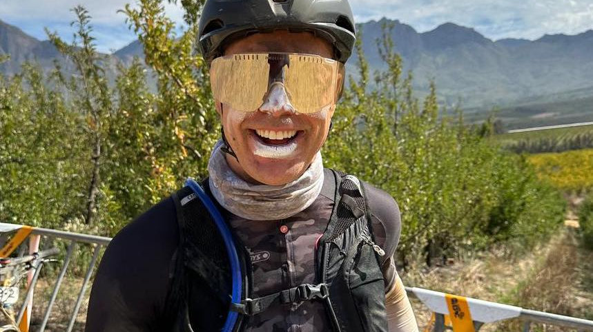 Absa Cape Epic 2024 Aid Station rider smiling and wearing sunscreen and sunglasses