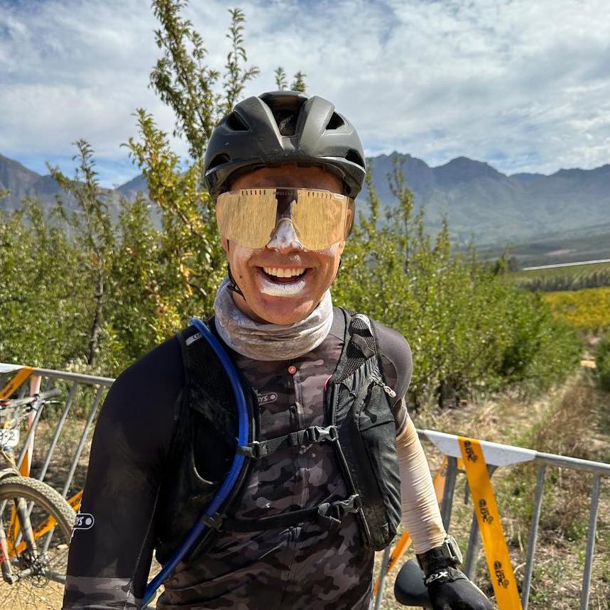 Absa Cape Epic 2024 Aid Station rider smiling and wearing sunscreen and sunglasses